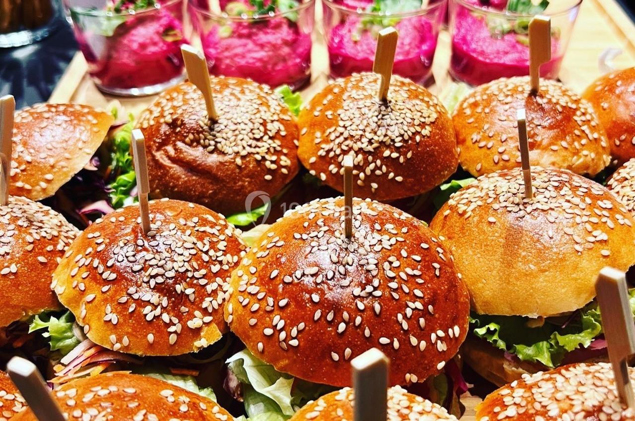 Mini burgers garnis de salade et servis avec des verrines de houmous rose en arrière-plan.