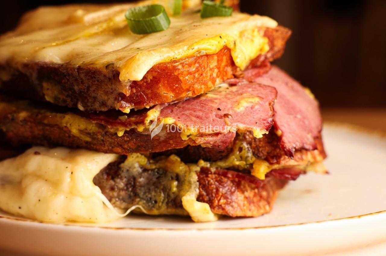 Sandwich chaud garni de viande fumée, fromage fondu et tranches de pain doré, décoré de rondelles d'oignon vert.