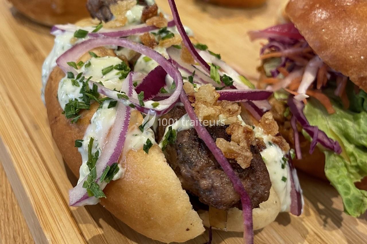 Sandwich garni de viande grillée, oignons rouges, sauce crémeuse, herbes fraîches et éclats croustillants sur pain moelleux.