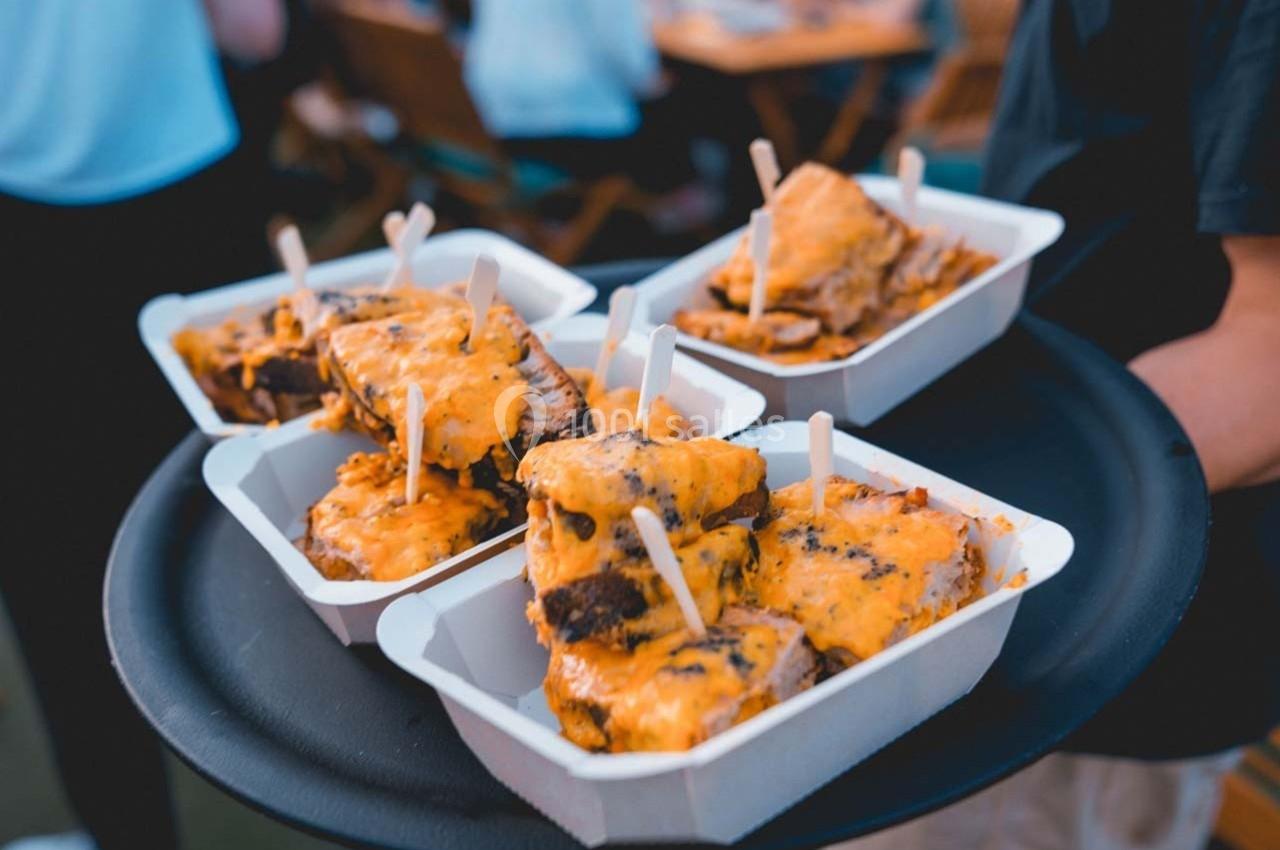 Plateau contenant plusieurs barquettes de plats garnis de fromage fondu, servis lors d'un événement en extérieur.