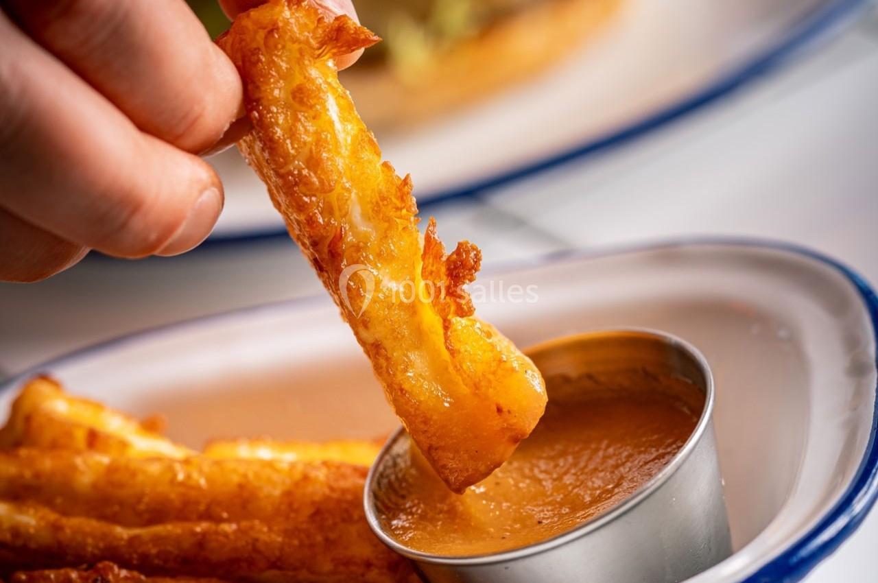 Frite dorée trempée dans une sauce crémeuse, servie dans une assiette blanche avec un ramequin en métal.
