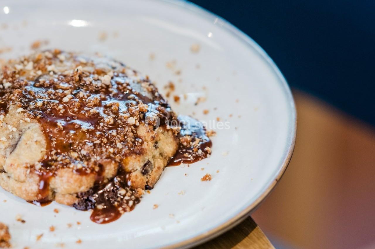 Un cookie aux pépites de chocolat nappé de caramel et saupoudré de miettes, présenté sur une assiette blanche.