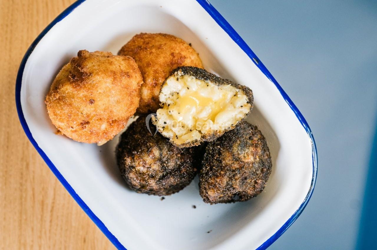 Boulettes panées dorées et noires, l'une ouverte révélant un cœur fondant au fromage, servies dans un plat blanc.
