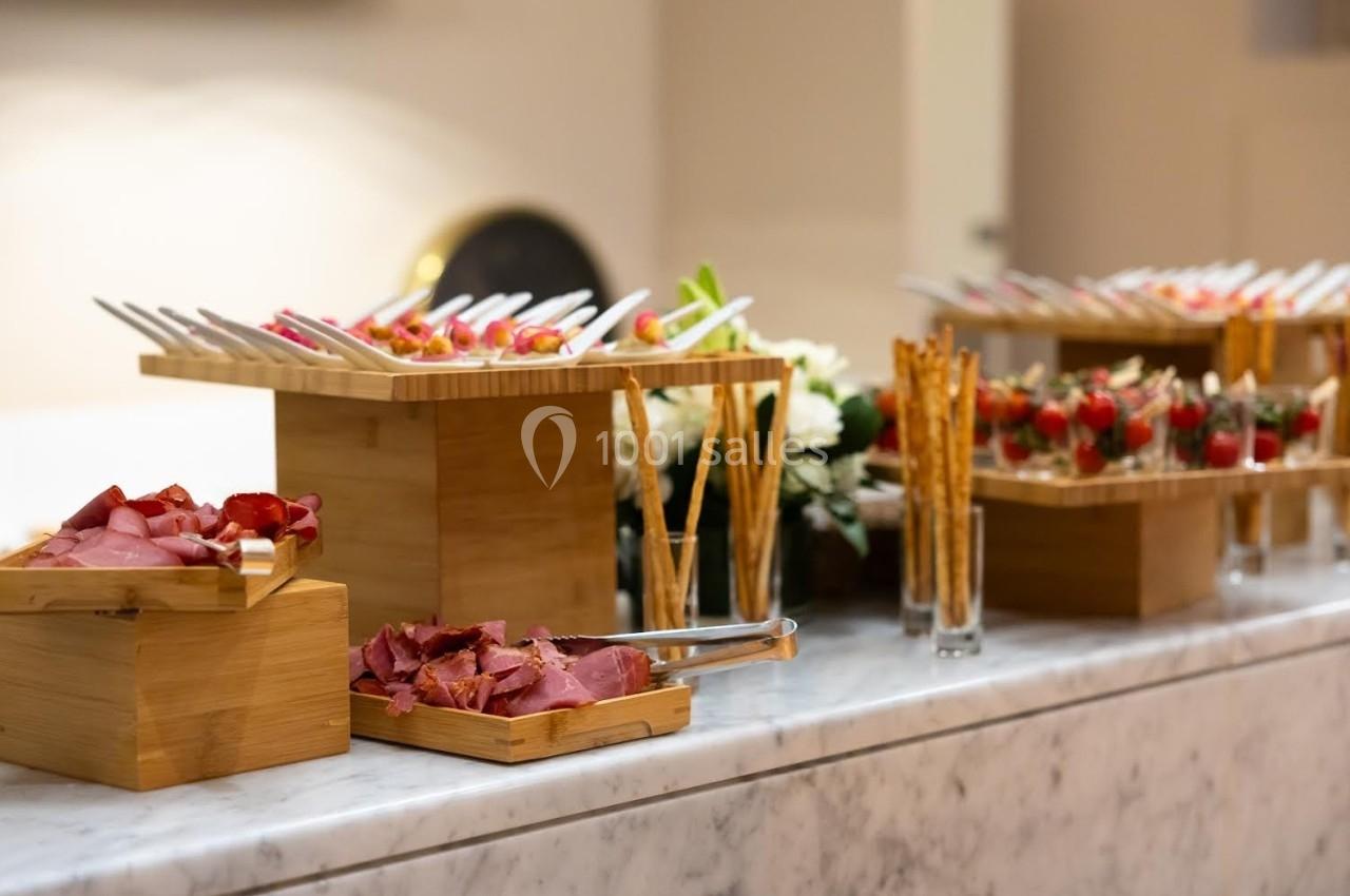 Buffet avec charcuterie, brochettes et gressins disposés sur des présentoirs en bois sur une table en marbre.