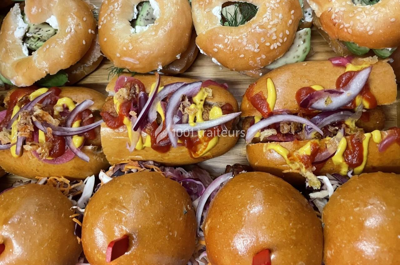Assortiment de hot-dogs garnis de sauces, oignons et condiments, entourés de bagels et petits pains.
