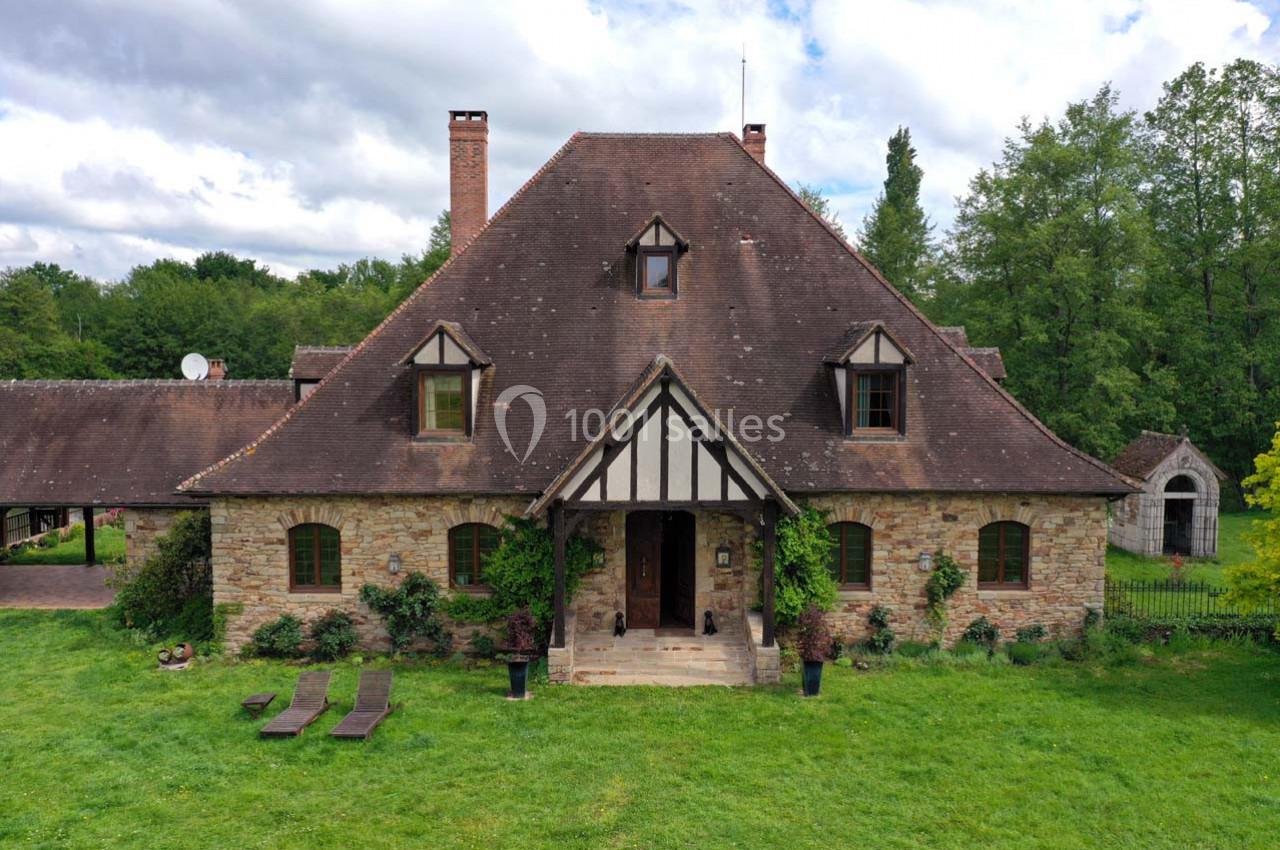 Maison en pierre avec toit en pente, entourée de verdure, avec une entrée centrale et des fenêtres mansardées.