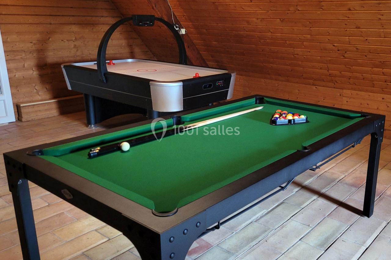 Table de billard avec accessoires au premier plan et table de hockey sur air en arrière-plan dans une pièce en bois.