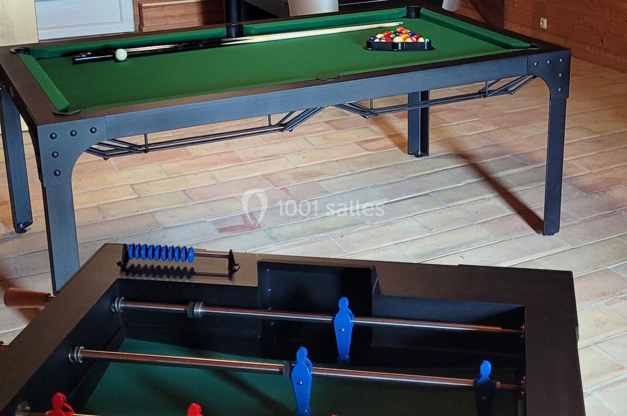 Table de billard avec triangle de billes colorées en arrière-plan et baby-foot en premier plan dans une pièce.