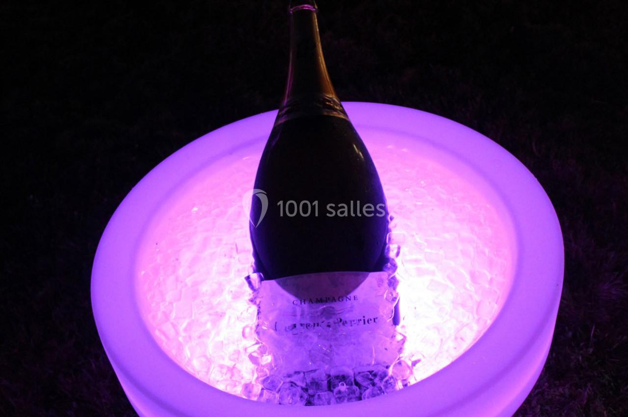 Bouteille de champagne posée dans un seau lumineux rempli de glace, éclairée par une lumière violette.