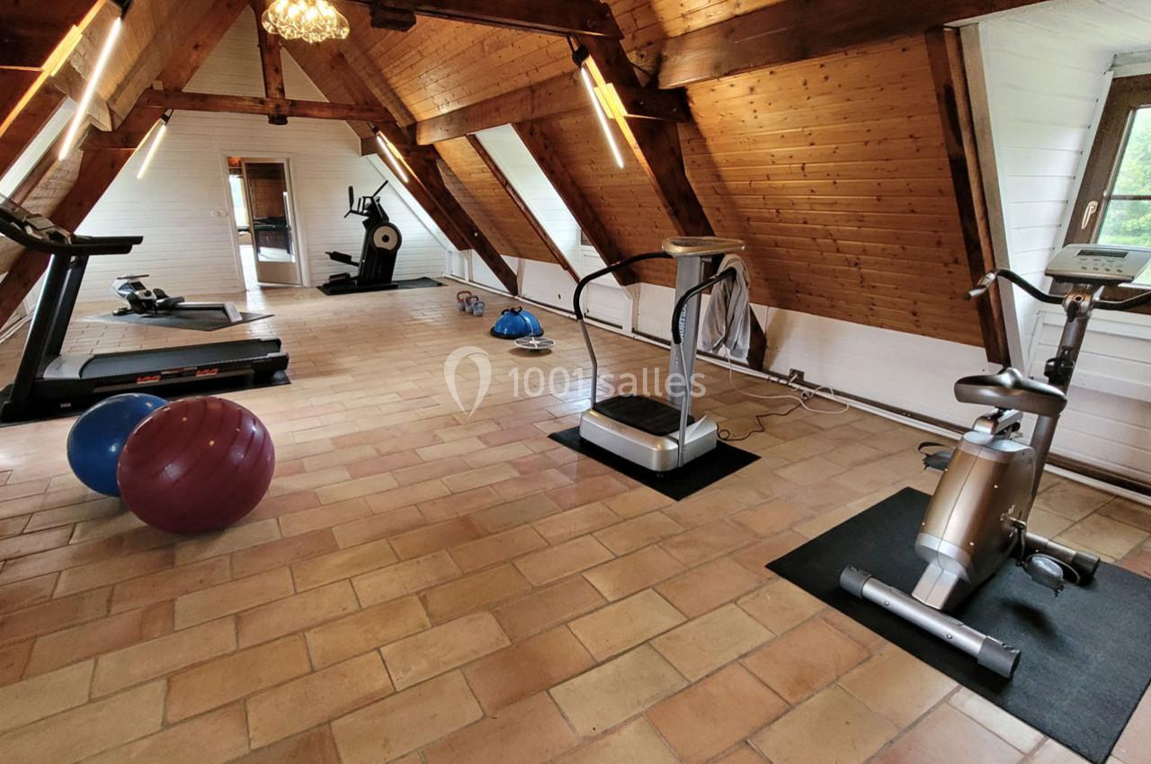 Salle de sport sous combles avec équipements tels que tapis de course, vélo d'appartement et ballons d'exercice.