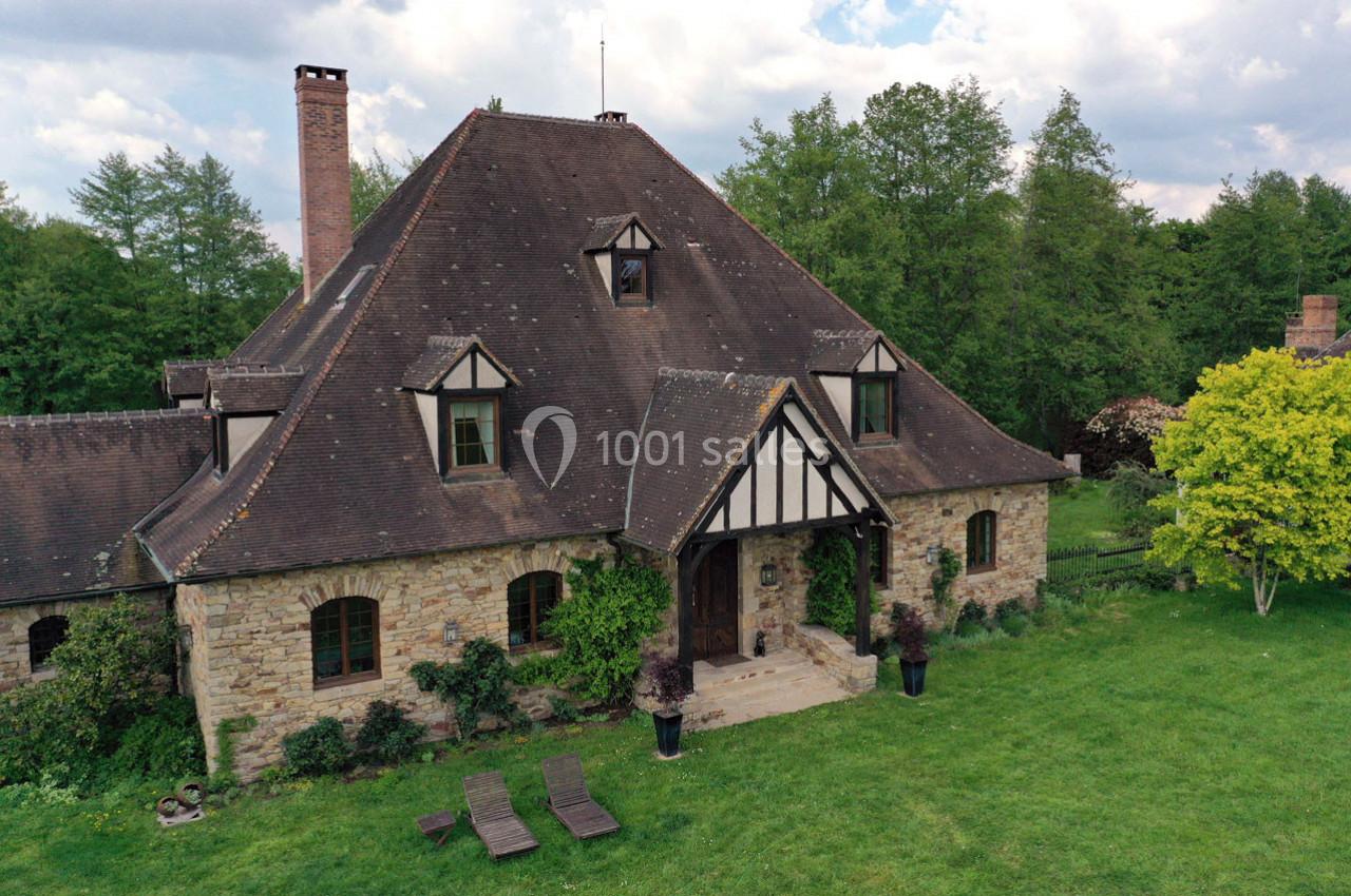 Maison en pierre avec toit en pente et colombages, entourée de verdure et d'un jardin avec chaises longues.
