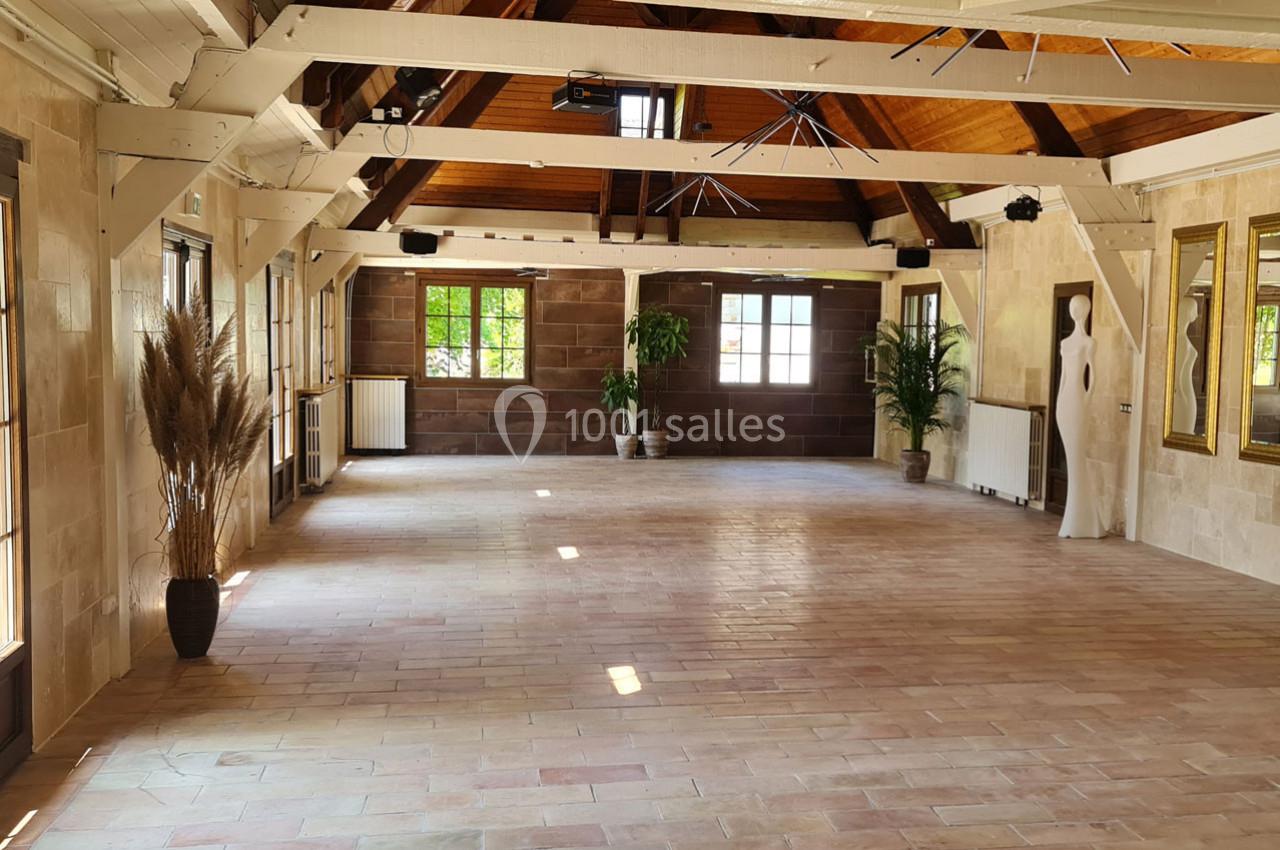 Salle lumineuse avec poutres apparentes, grandes fenêtres, plantes décoratives et statue blanche sur un sol en terre cuite.