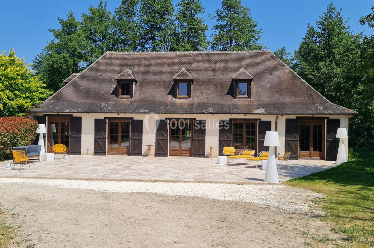 Maison traditionnelle avec toit en pente, terrasse aménagée de mobilier extérieur, entourée de verdure.