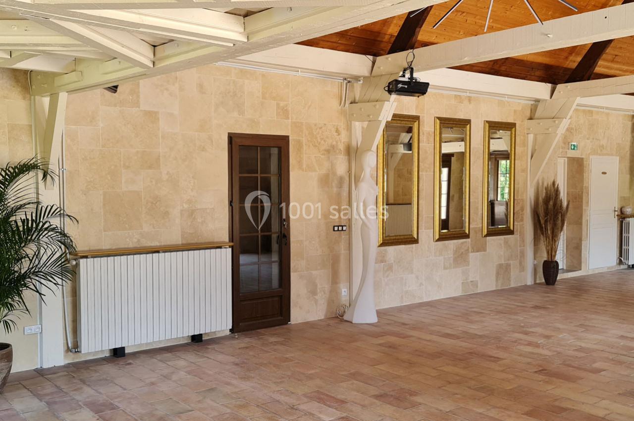 Salle lumineuse avec murs en pierre, sol en carrelage, poutres apparentes, miroirs dorés et plantes décoratives.