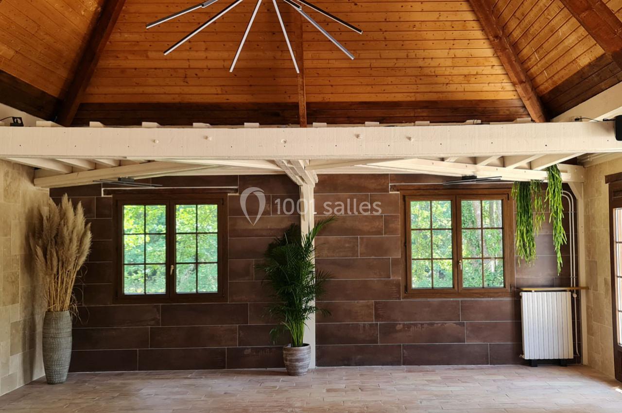 Salle lumineuse avec plafond en bois, murs en pierre et carrelage, deux fenêtres, plantes décoratives et radiateur.