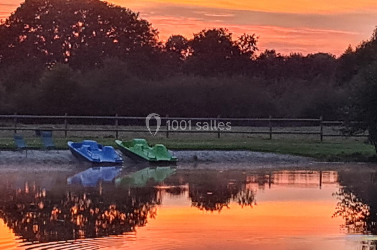 Deux pédalos bleus et verts stationnés au bord d'un étang reflétant un ciel de coucher de soleil orangé.