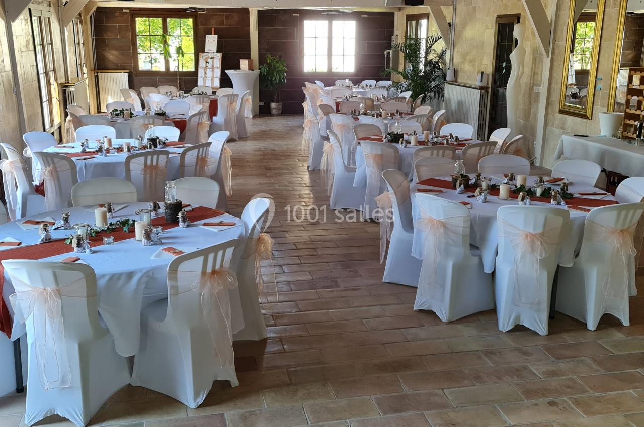 Salle de réception lumineuse avec tables rondes décorées de nappes blanches, chemins de table orange et chaises assorties.