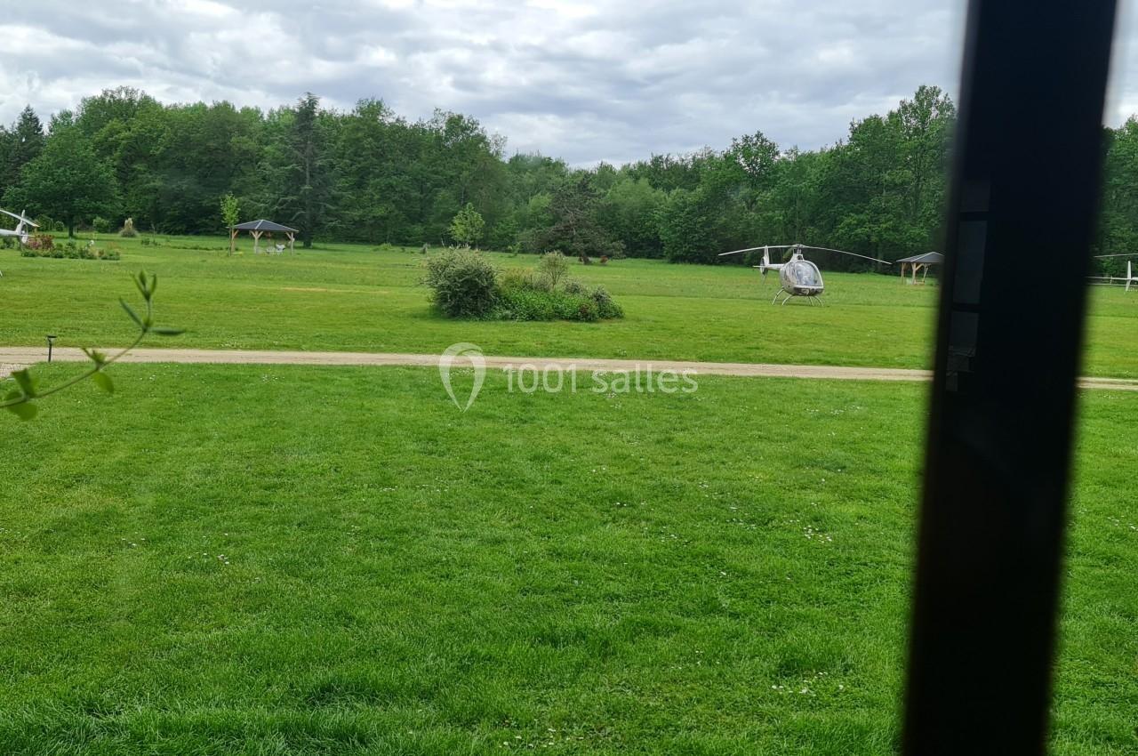 Deux hélicoptères stationnés sur une pelouse verte entourée d'arbres sous un ciel nuageux.