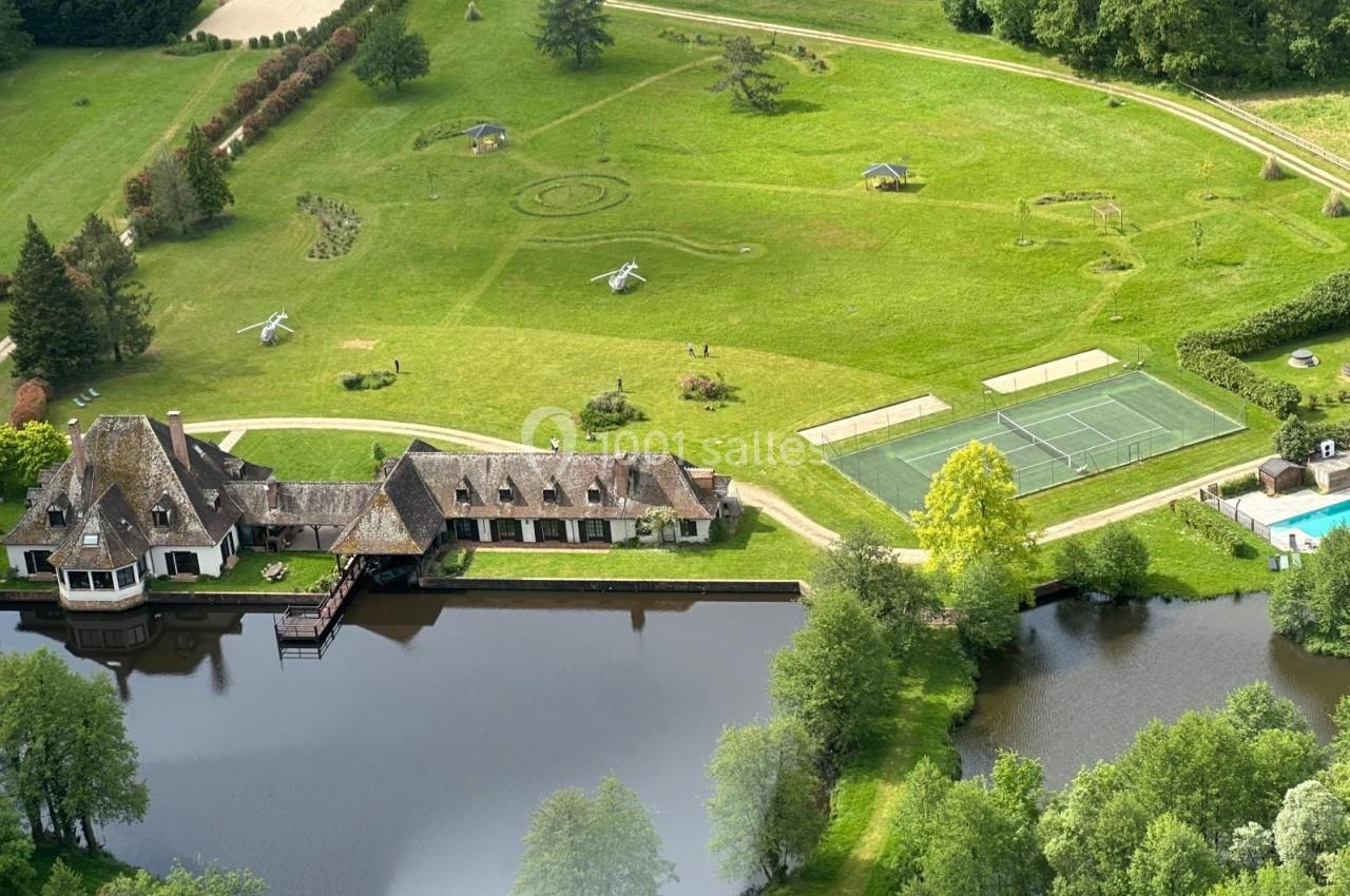 Vue aérienne d'une propriété avec maison, étang, courts de tennis, piscine et vaste jardin paysager.