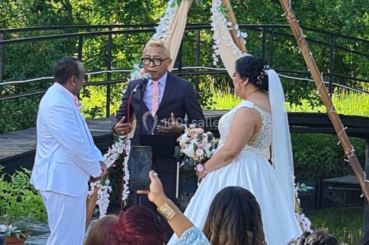Un couple échange ses vœux devant un officiant lors d'une cérémonie de mariage en plein air.