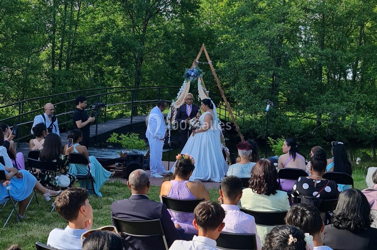 Cérémonie de mariage en plein air avec des invités assis, un couple échangeant ses vœux devant une arche décorée.