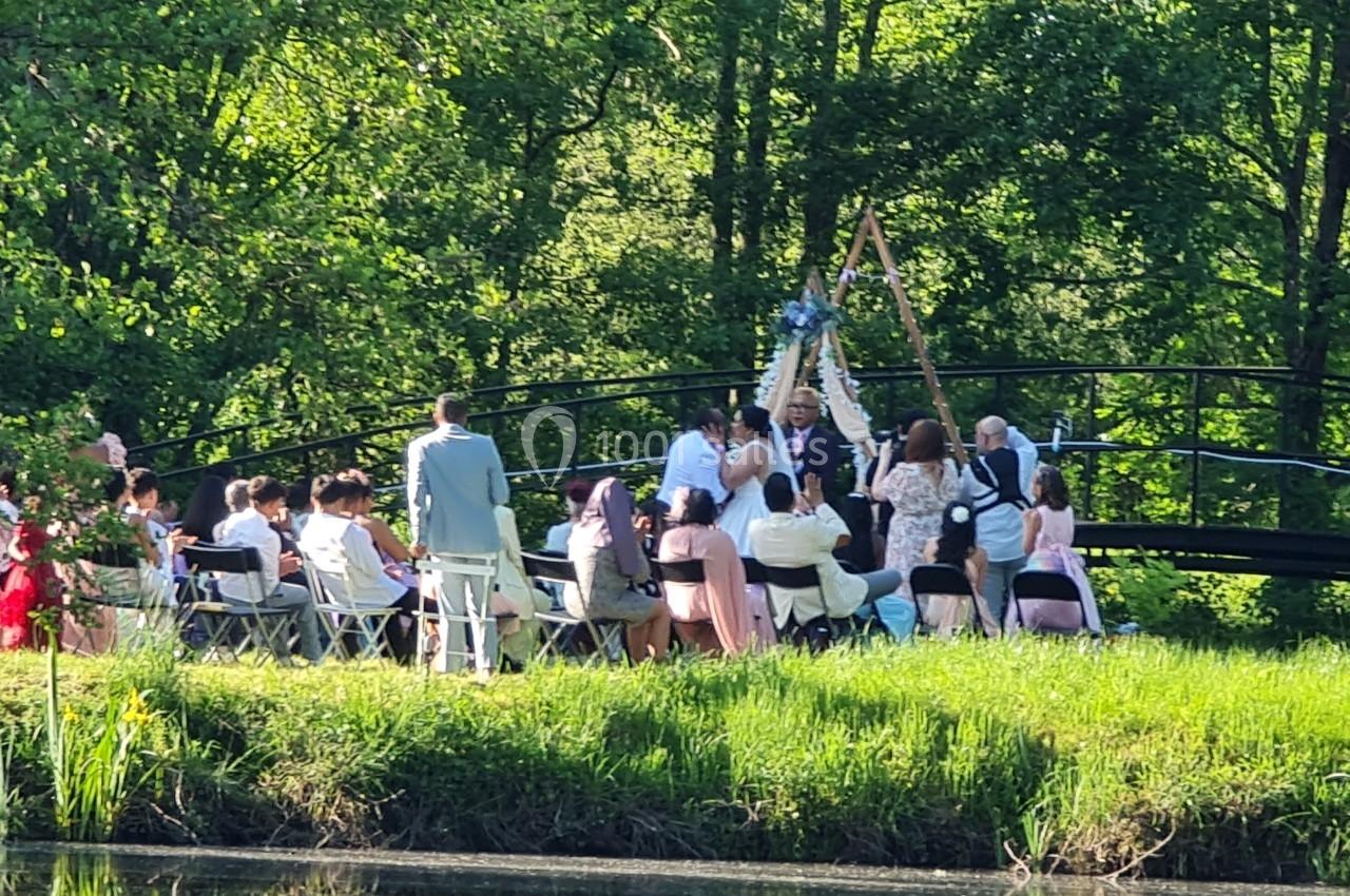 Un groupe de personnes assises en extérieur près d'un pont, lors d'une cérémonie dans un cadre verdoyant.
