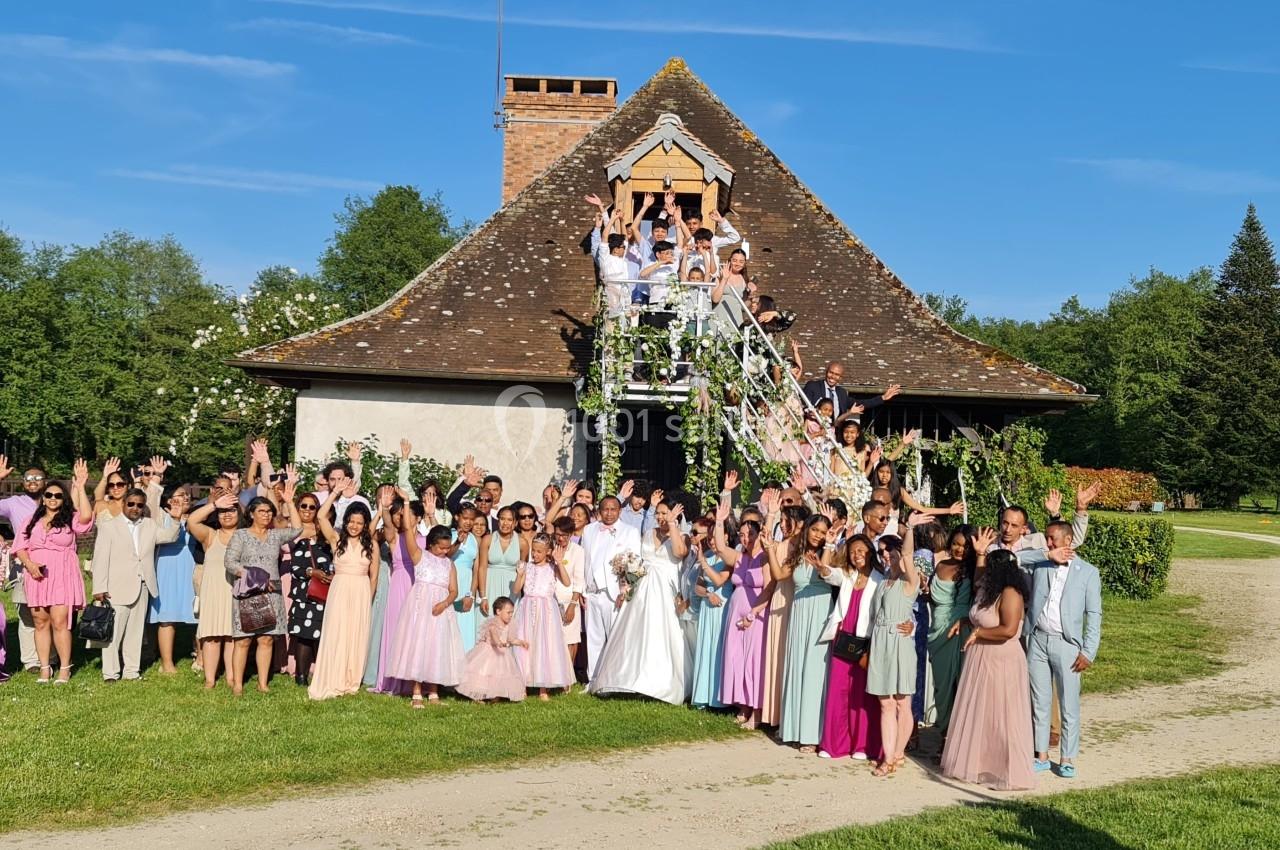 Groupe de personnes en tenue festive posant devant une maison avec un escalier extérieur, entourée de verdure.