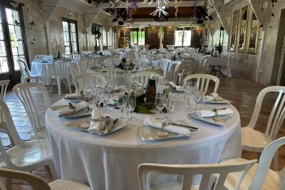 Salle de réception décorée avec des tables rondes dressées, nappes blanches, verres et couverts élégants.