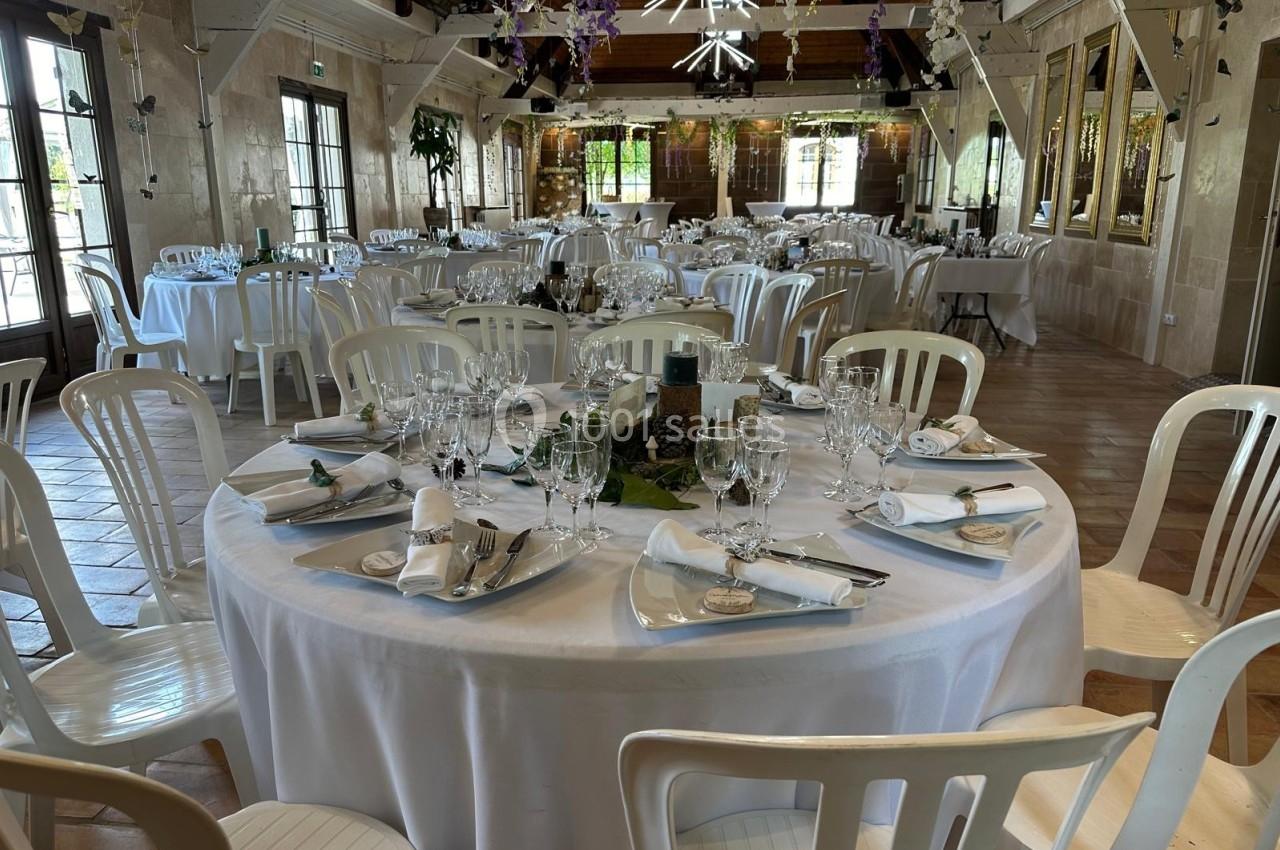 Salle de réception décorée avec des tables rondes dressées, nappes blanches, verres et couverts élégants.