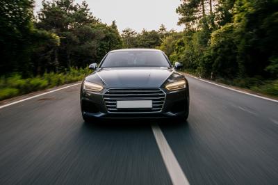 Voiture noire roulant sur une route bordée d'arbres, vue de face au niveau du sol.