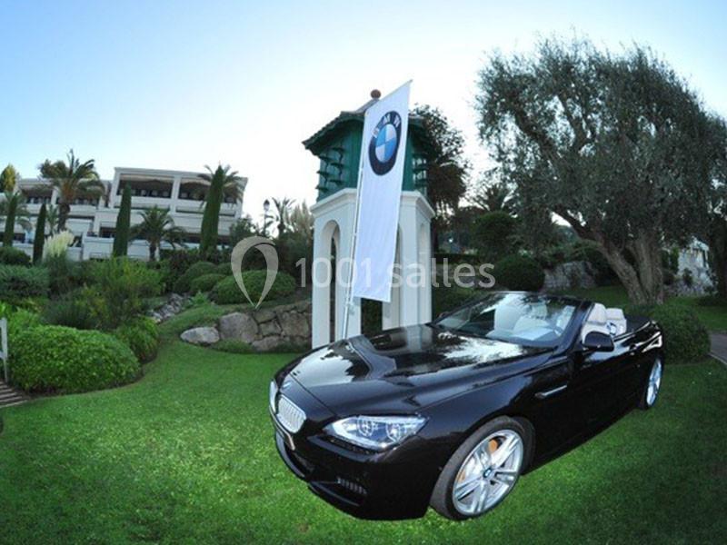Voiture décapotable noire stationnée sur une pelouse devant un bâtiment avec un drapeau BMW.