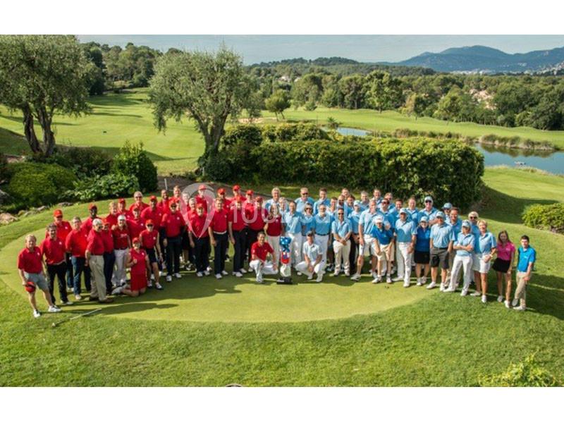 Un grand groupe de personnes en tenue rouge et bleue posant sur un terrain de golf entouré de verdure.