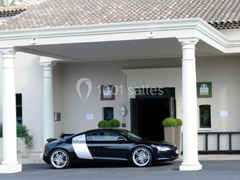 Voiture de sport noire garée devant l'entrée d'un bâtiment avec colonnes blanches et toit en tuiles.