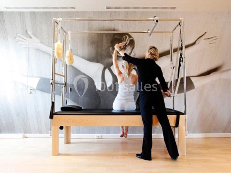 Une femme en tenue de sport pratique des exercices sur un appareil de Pilates, guidée par une instructrice.