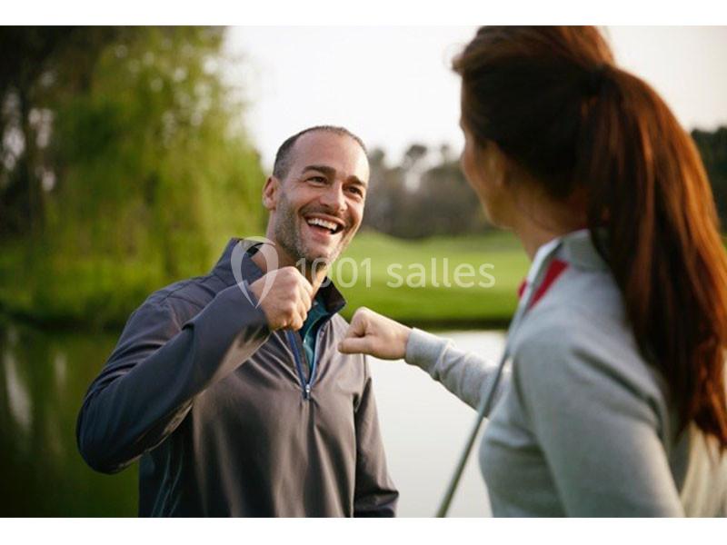 Deux personnes souriantes échangent un geste de poing contre poing près d'un plan d'eau dans un cadre verdoyant.
