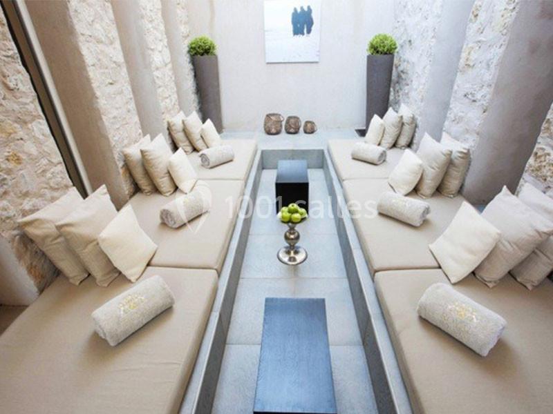 Banquette beige entourant une table basse dans un espace lumineux avec murs en pierre et décoration minimaliste.