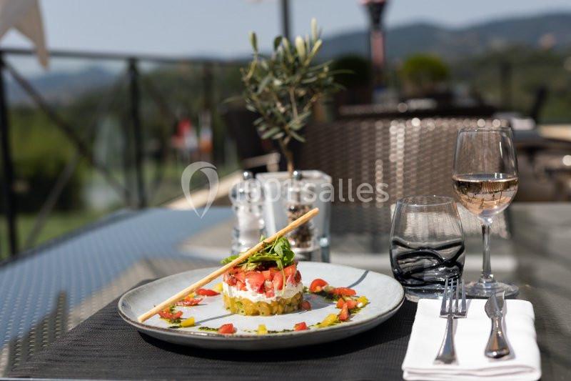 Assiette de tartare coloré avec couverts, verre de vin et décor de terrasse en arrière-plan.