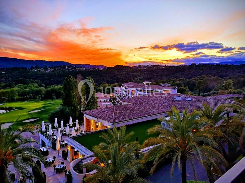 Vue d'un complexe hôtelier entouré de palmiers et d'un paysage vallonné au coucher du soleil.