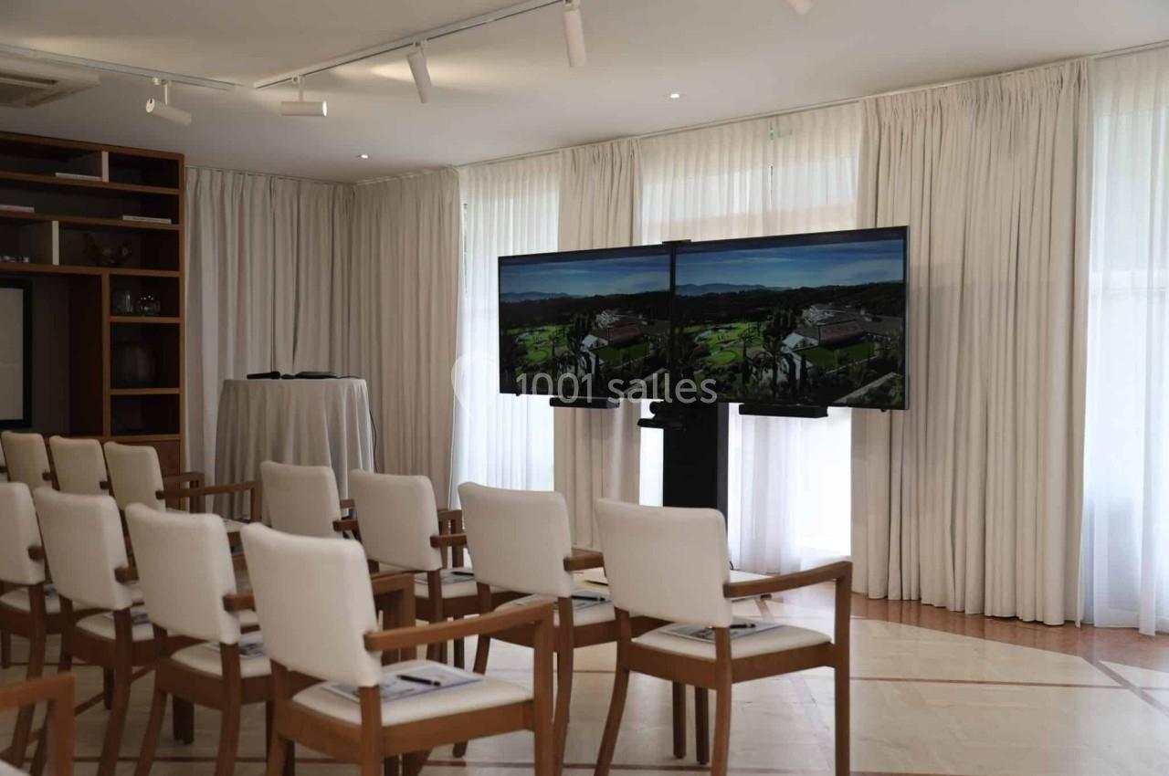 Salle de conférence lumineuse avec des chaises alignées et deux écrans affichant un paysage.