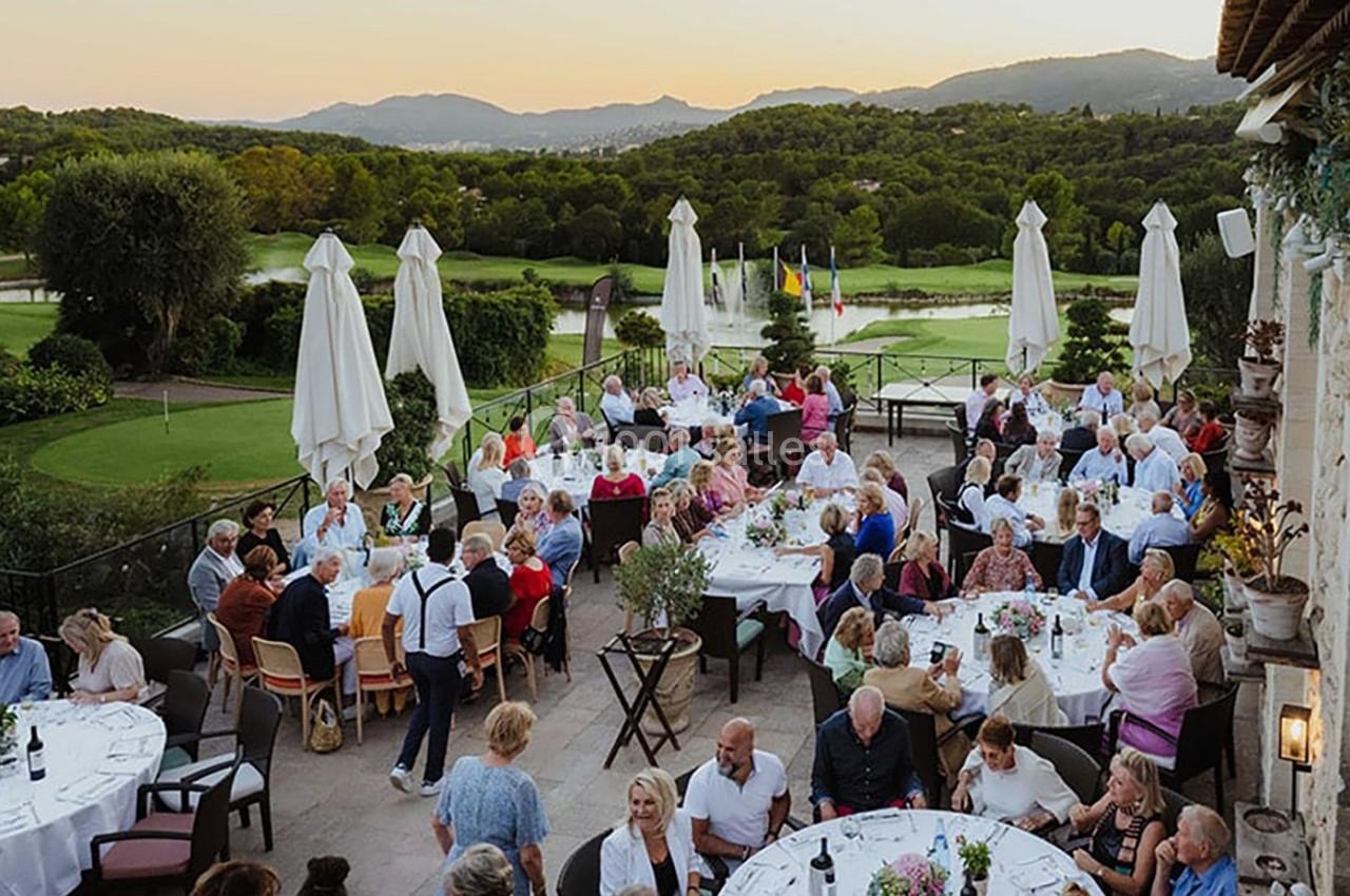 Groupe de personnes dînant en plein air sur une terrasse avec vue sur un paysage verdoyant et des collines au coucher du…