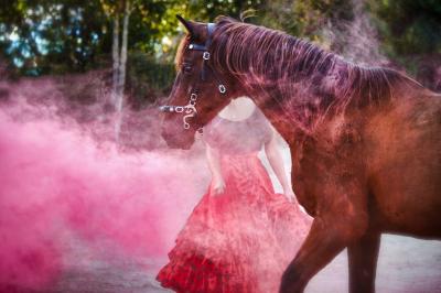 Une femme crache du feu dans l'obscurité, tenant une torche allumée, avec un cheval en arrière-plan.