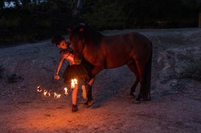 Une femme crache du feu dans l'obscurité, tenant une torche allumée, avec un cheval en arrière-plan.