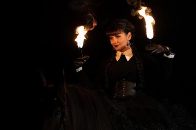 Une femme crache du feu dans l'obscurité, tenant une torche allumée, avec un cheval en arrière-plan.