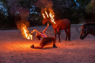Une femme crache du feu dans l'obscurité, tenant une torche allumée, avec un cheval en arrière-plan.
