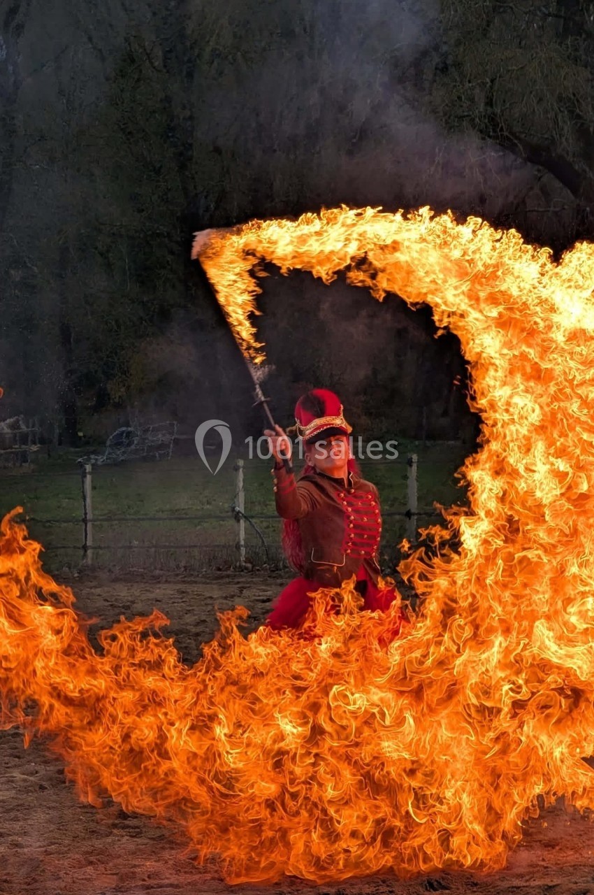 Une femme en costume rouge manipule un bâton enflammé, créant un arc de feu dans un espace extérieur.