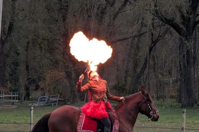 Femme en tenue traditionnelle caressant un cheval brun harnaché, dans un environnement naturel verdoyant.