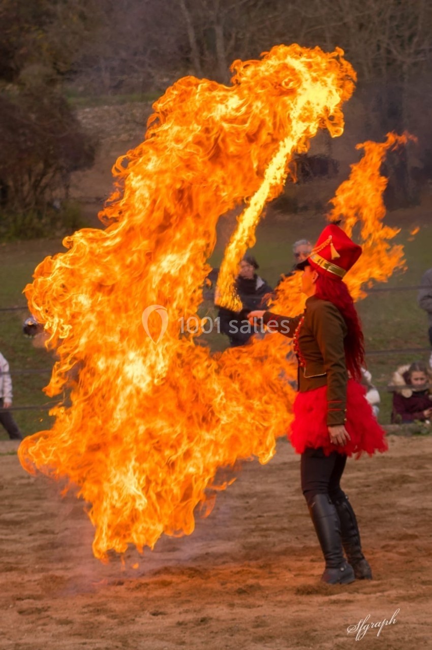 Une artiste en costume rouge manipule une grande flamme lors d'une performance en plein air.