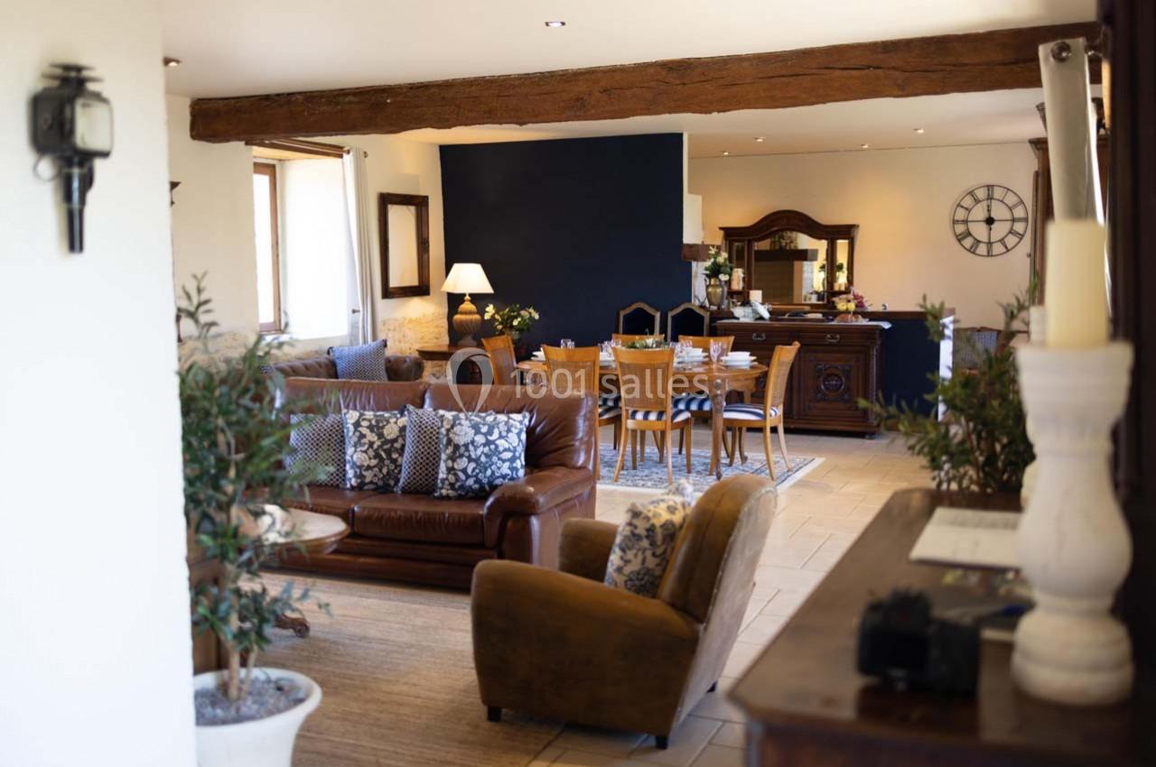 Salon lumineux avec poutres apparentes, canapé en cuir, fauteuils, table à manger et décoration chaleureuse.