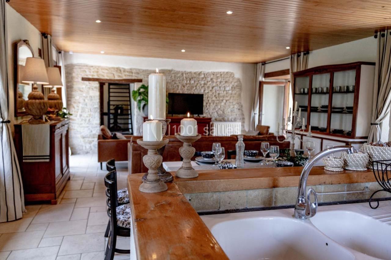 Vue d'une cuisine ouverte sur un salon avec murs en pierre, plafond en bois et décoration chaleureuse.