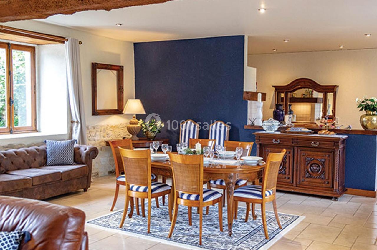Salle à manger avec table en bois, chaises à rayures, buffet ancien, canapé et mur bleu dans un intérieur lumineux.